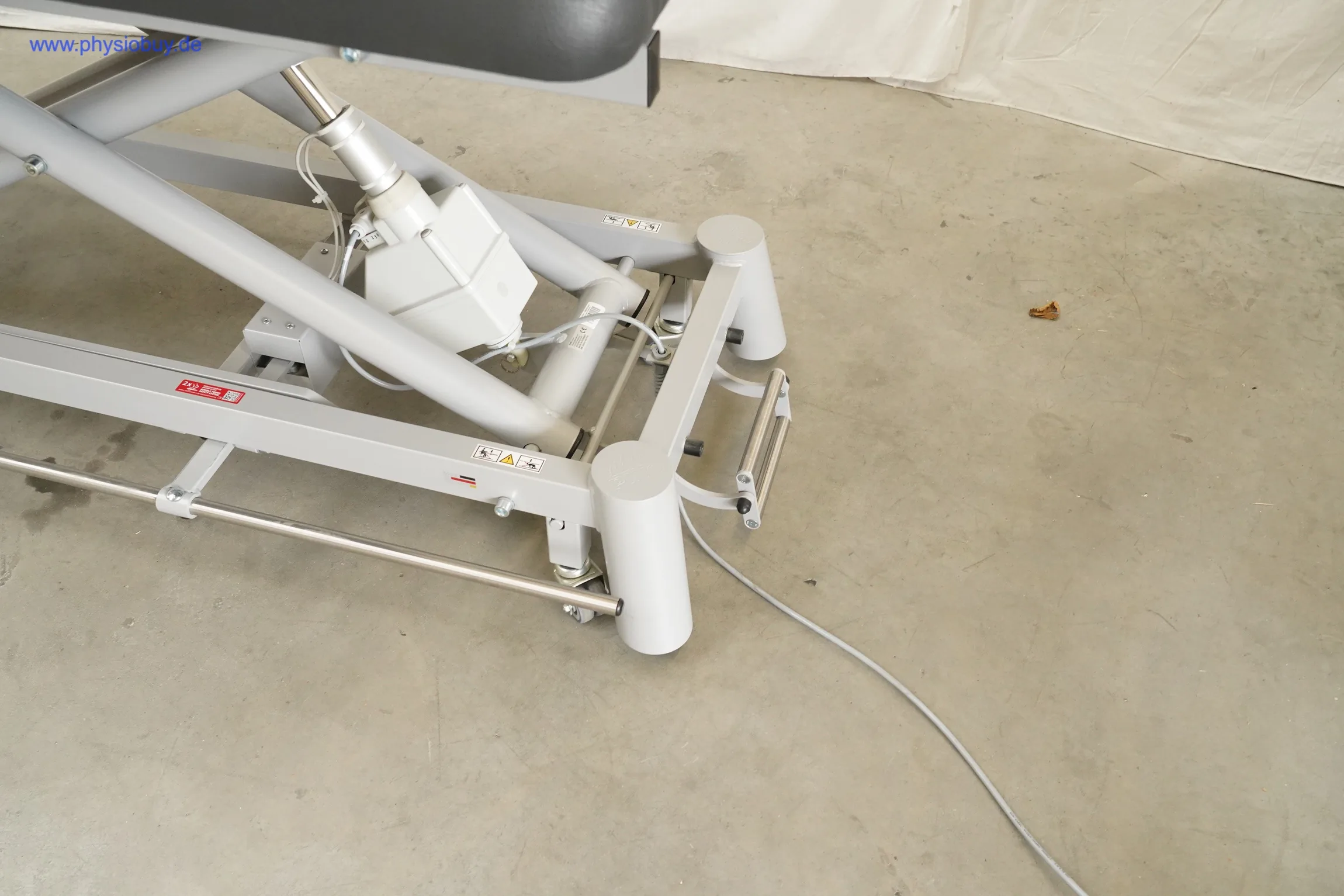 PINO XPert+ Therapieliege, Untergestell mit Hubmechanismus und Elektromotor, Anschlusskabel liegt auf Betonboden
