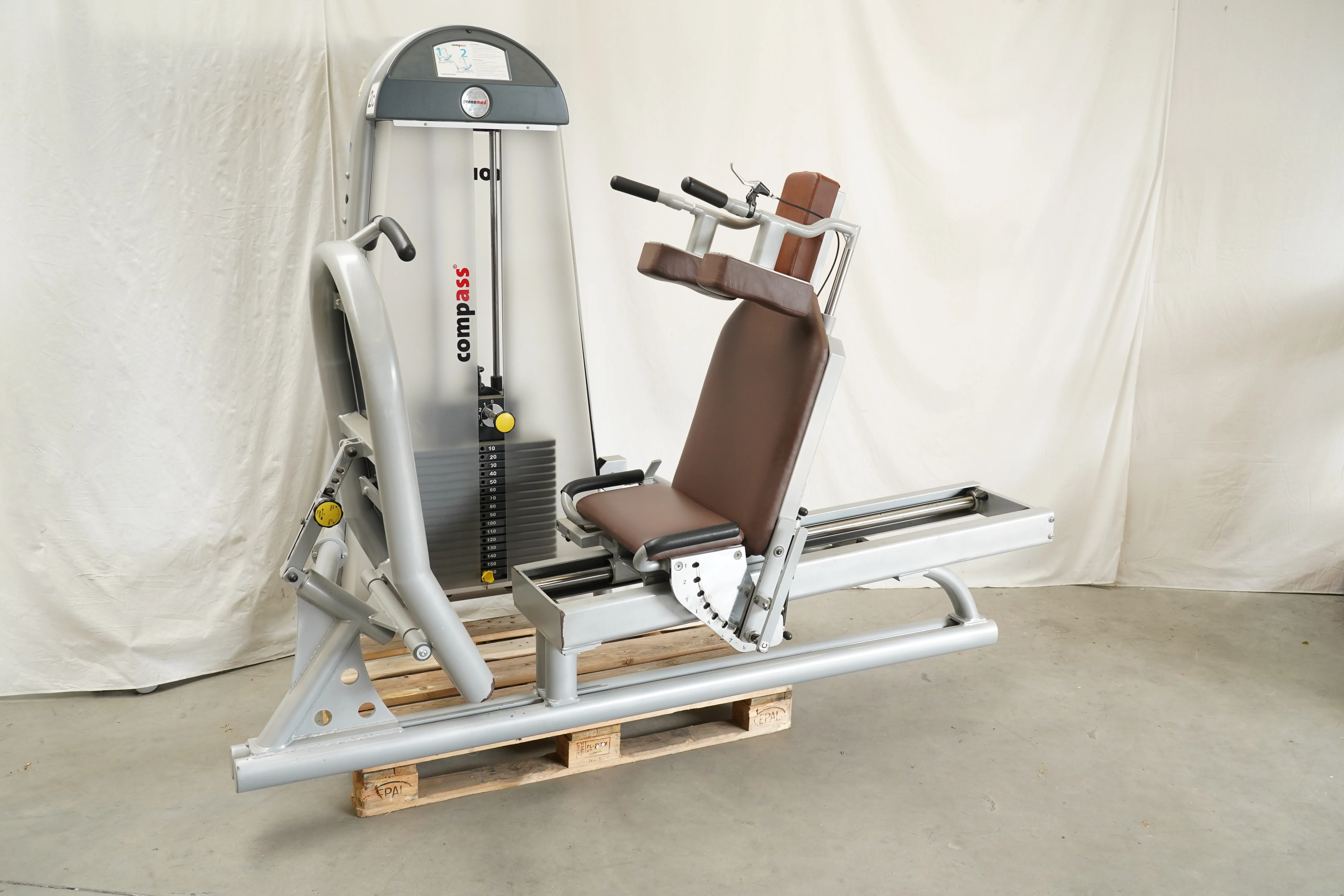Proxomed Compass 530 KGG-Satz, Beinpresse mit braunem Sitzpolster und Gewichtsblock, schräg von vorn auf einer Palette