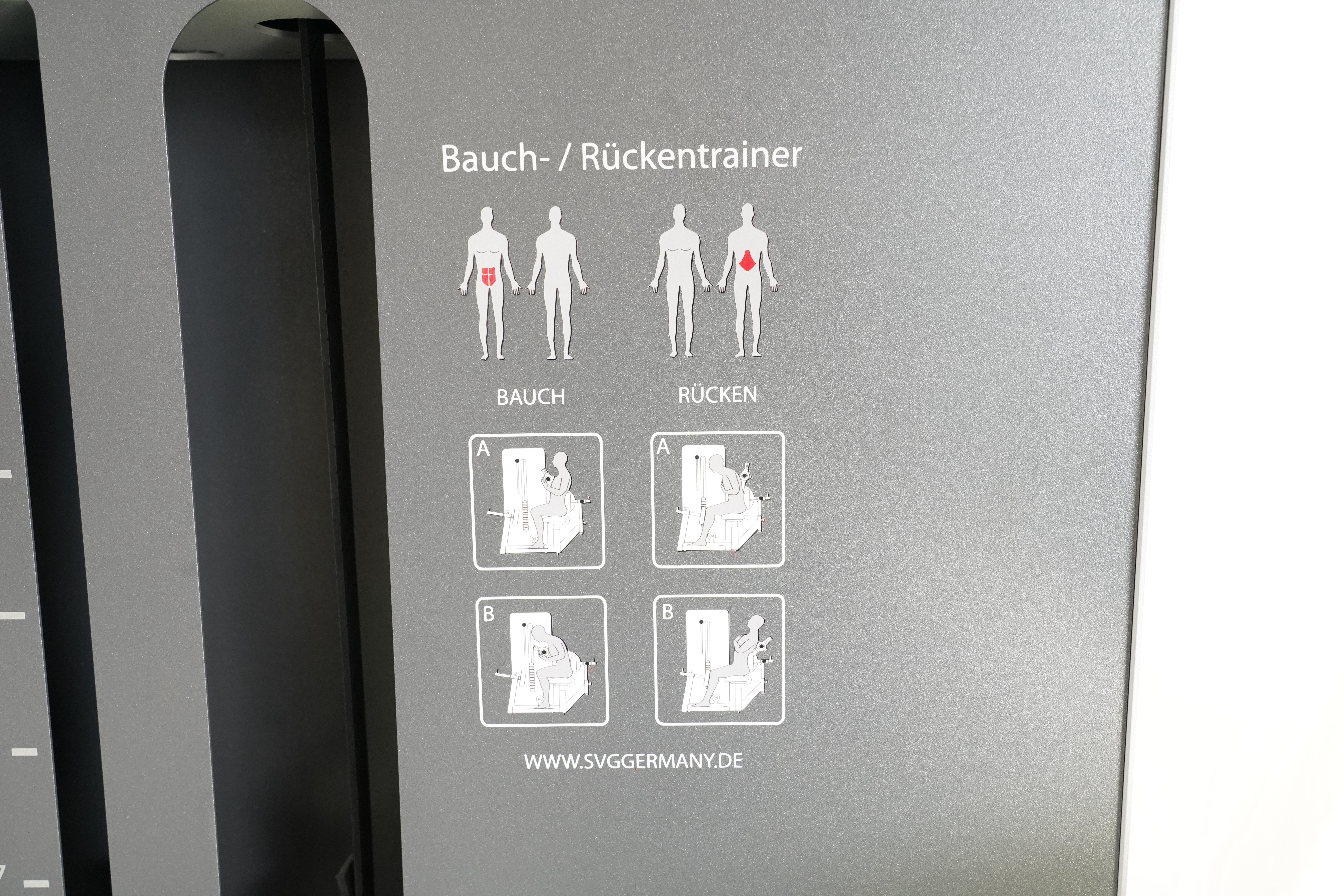 SVG RehaLine 2.0 KG-Gerätesatz: Beschriftung Bauch-/Rückentrainer mit Piktogrammen auf grauer Verkleidung