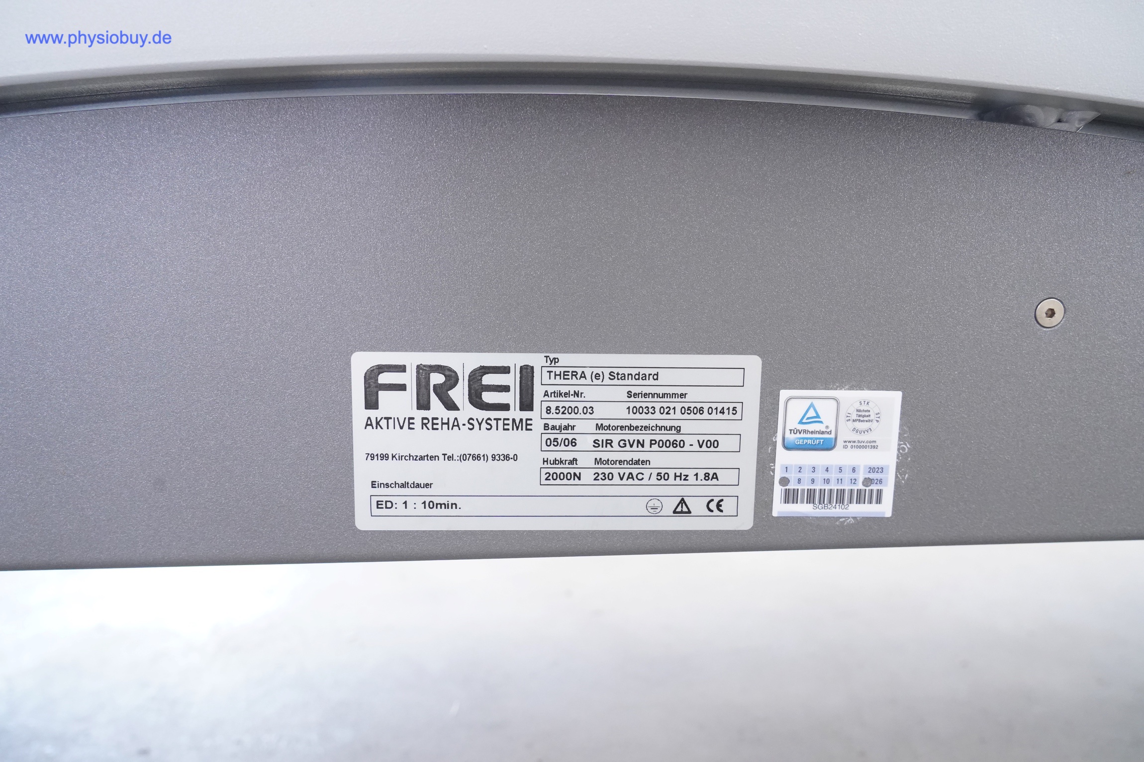 Typenschild der FREI THERA Standard Therapieliege auf grauer Verkleidung mit Prüfzeichen und Angaben zur Spannung