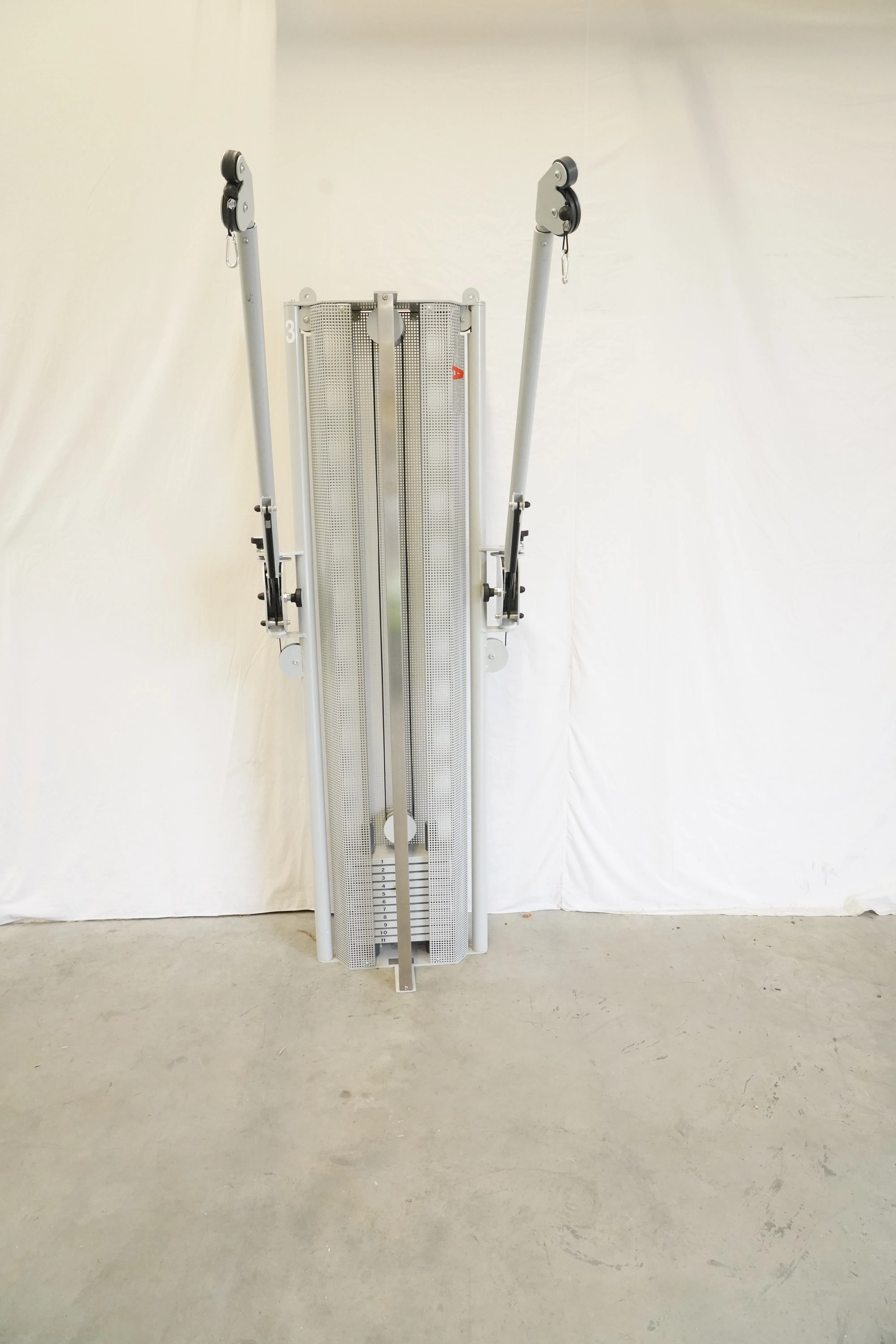 Stolzenberg Cable Cross Wandzugapparat von vorn mit perforierter Verkleidung und zwei hochgestellten Armen mit Umlenkrollen
