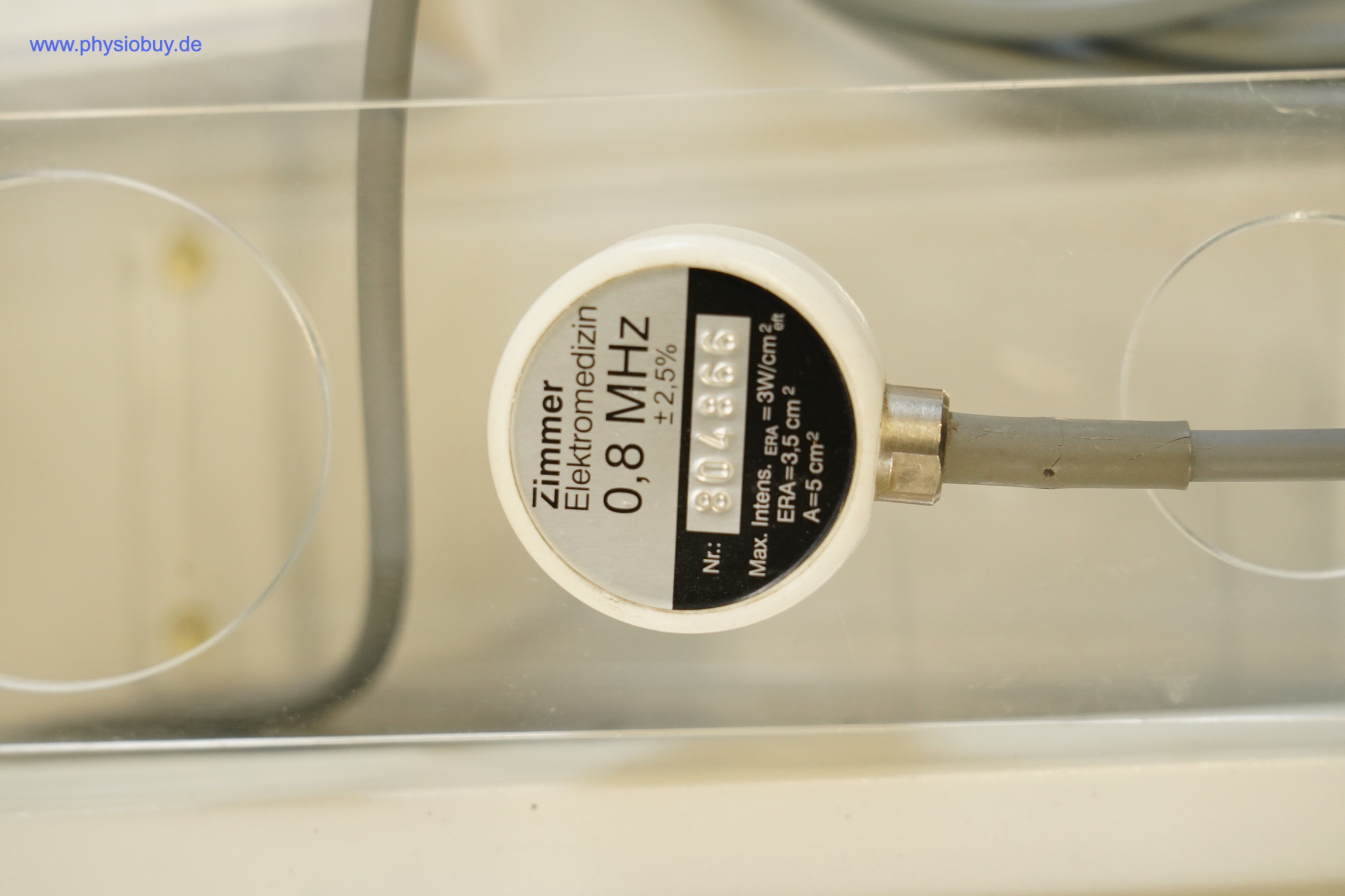 Zimmer SonoStim Ultraschallkopf mit Typenschild 0,8 MHz und grauem Anschlusskabel auf transparenter Ablage, Draufsicht
