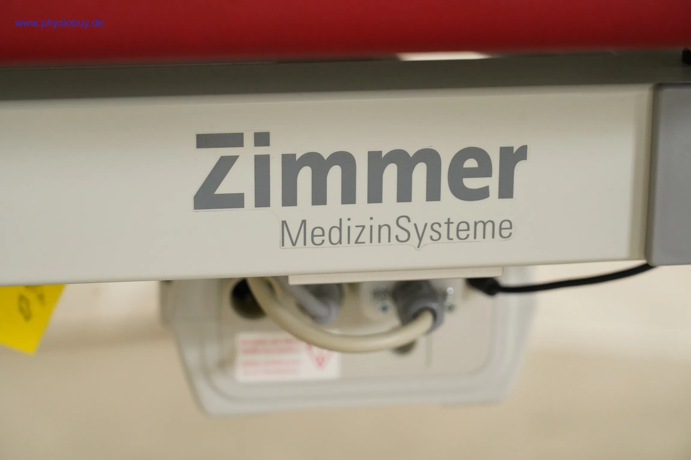 Zimmer Axion Behandlungsliege: Zimmer-MedizinSysteme-Schriftzug am Rahmen, darunter Antriebsgehäuse mit Kabel