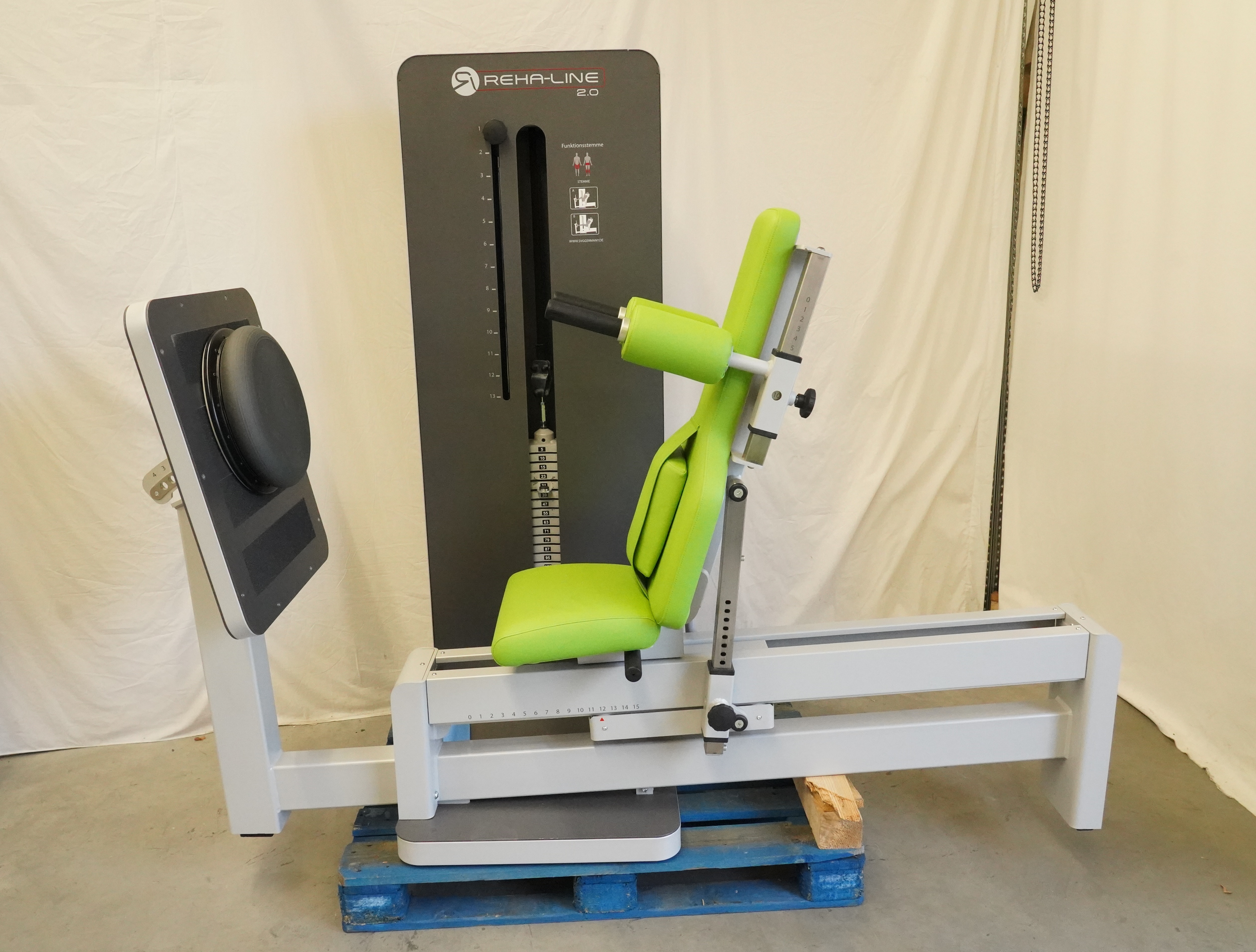 SVG RehaLine 2.0 KG-Gerätesatz seitlich: Beinpresse mit grünem Sitz, Rückenlehne, Fußplatte und Gewichtsblock auf Holzpalette