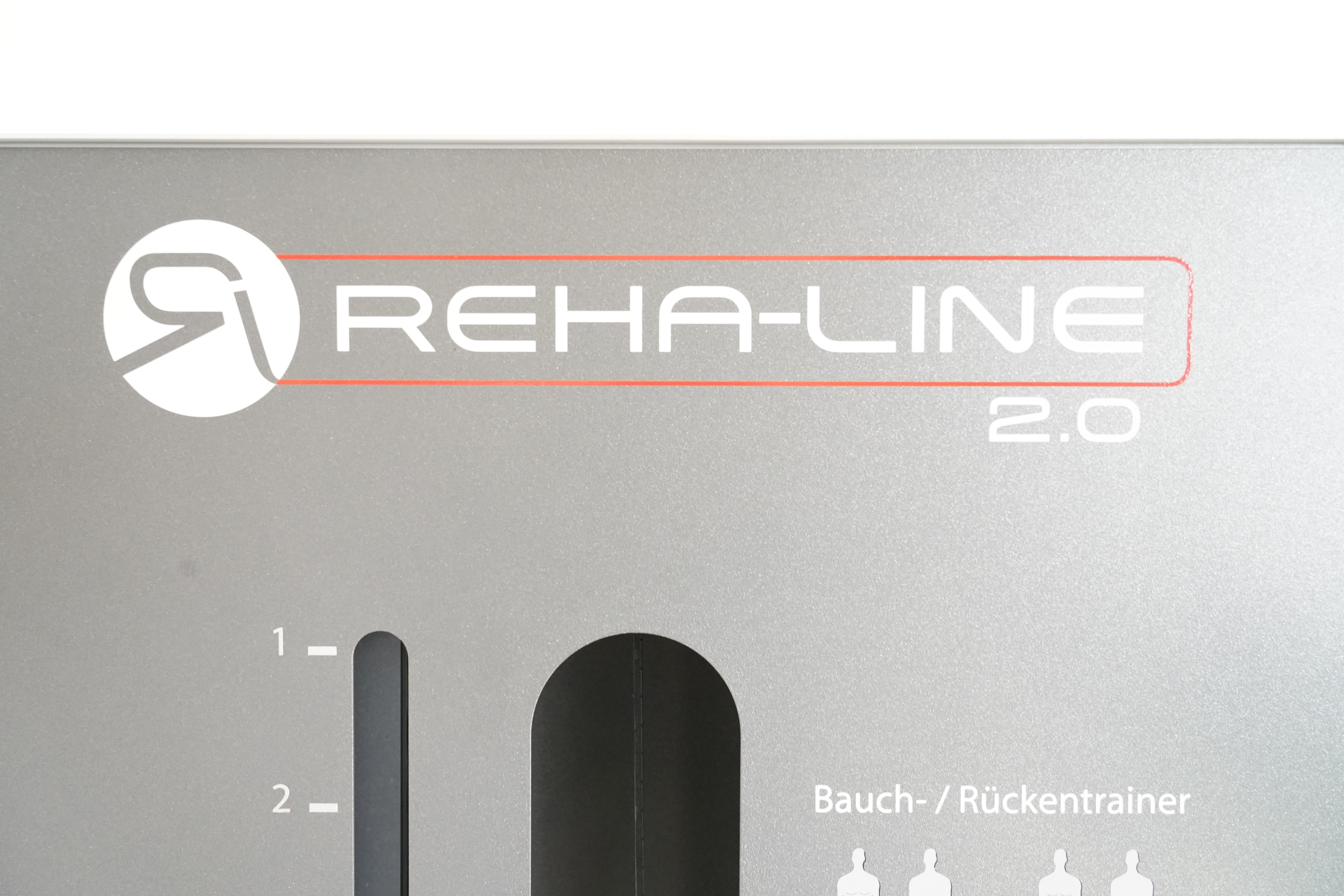 SVG RehaLine 2.0 KG-Gerätesatz: Logo Reha-Line 2.0 auf grauer Blende, darunter Skala und Beschriftung Bauch-/Rückentrainer