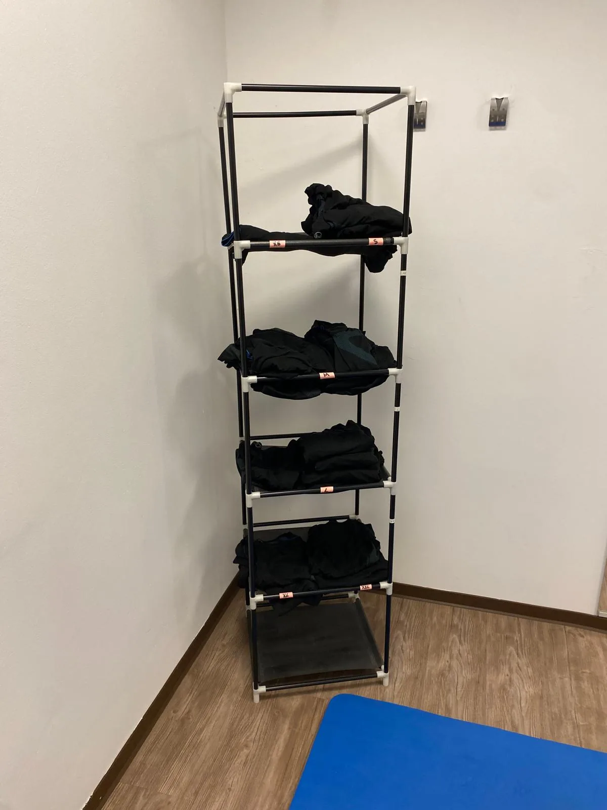 Ablageregal mit mehreren gefalteten EMS-Westen des miha-bodytec-Sets in einer Zimmerecke