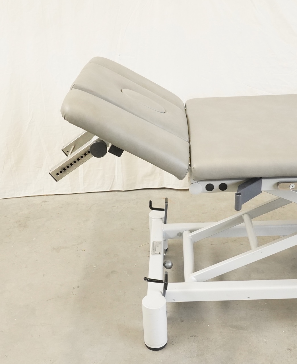FREI Gym-X (e) Manuell Therapieliege seitlich: hochgestelltes graues Kopfteil mit Lochschiene und weißes Gestell