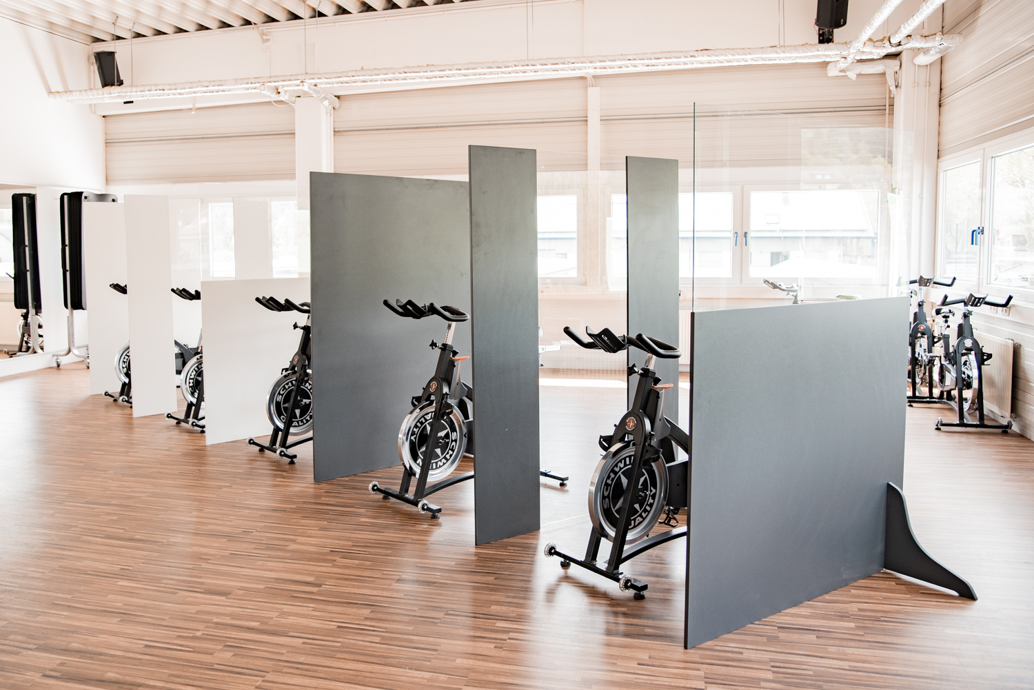 Reihe dunkler Trennwände Basic trennt Indoor-Cycles diagonal im lichtdurchfluteten Fitnessstudio