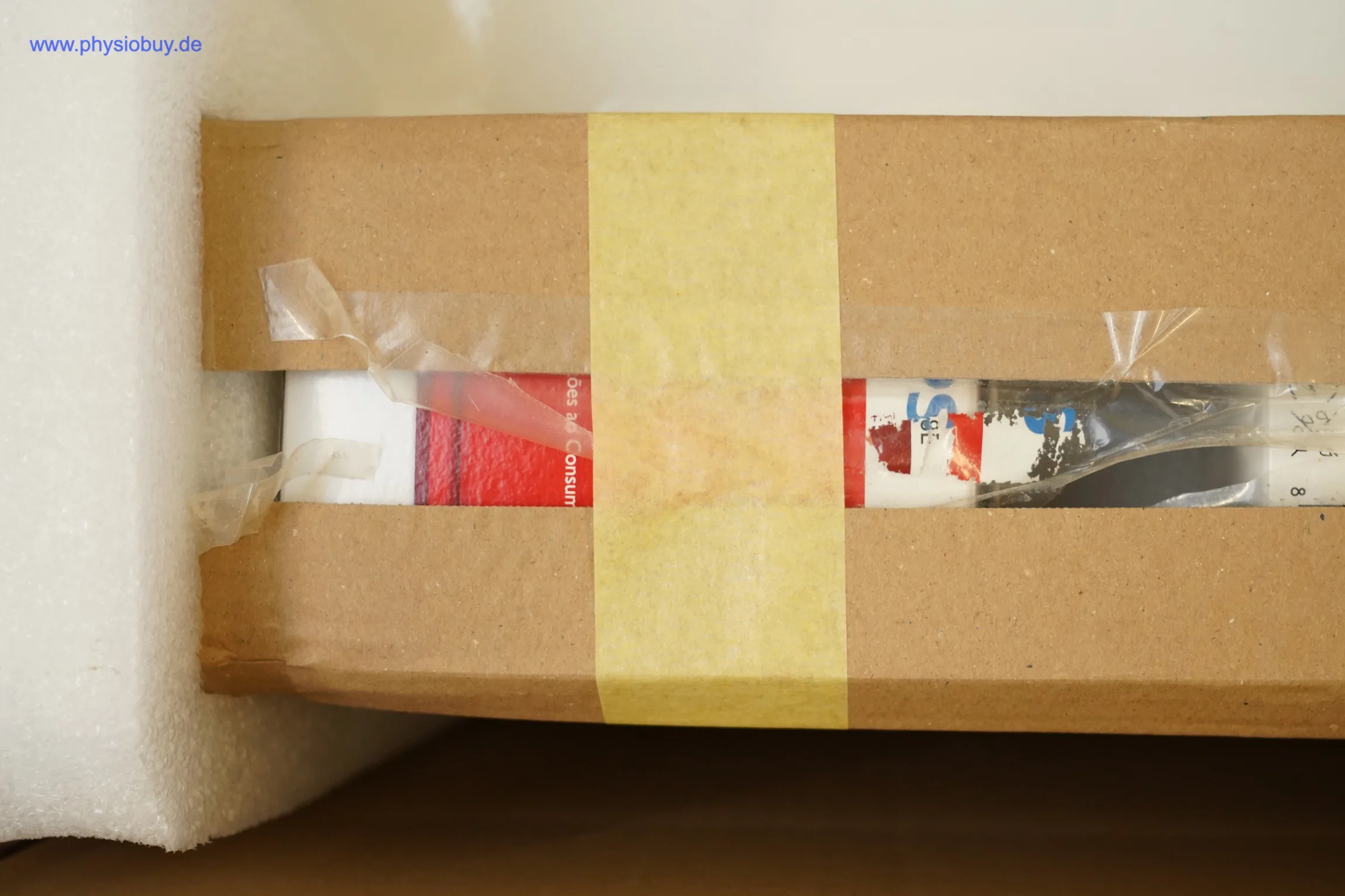 Verpackter Heuser Rotlicht Strahlerkopf TGS 6.2 in Karton mit gelbem Klebeband, daneben weißes Schaumstoffpolster