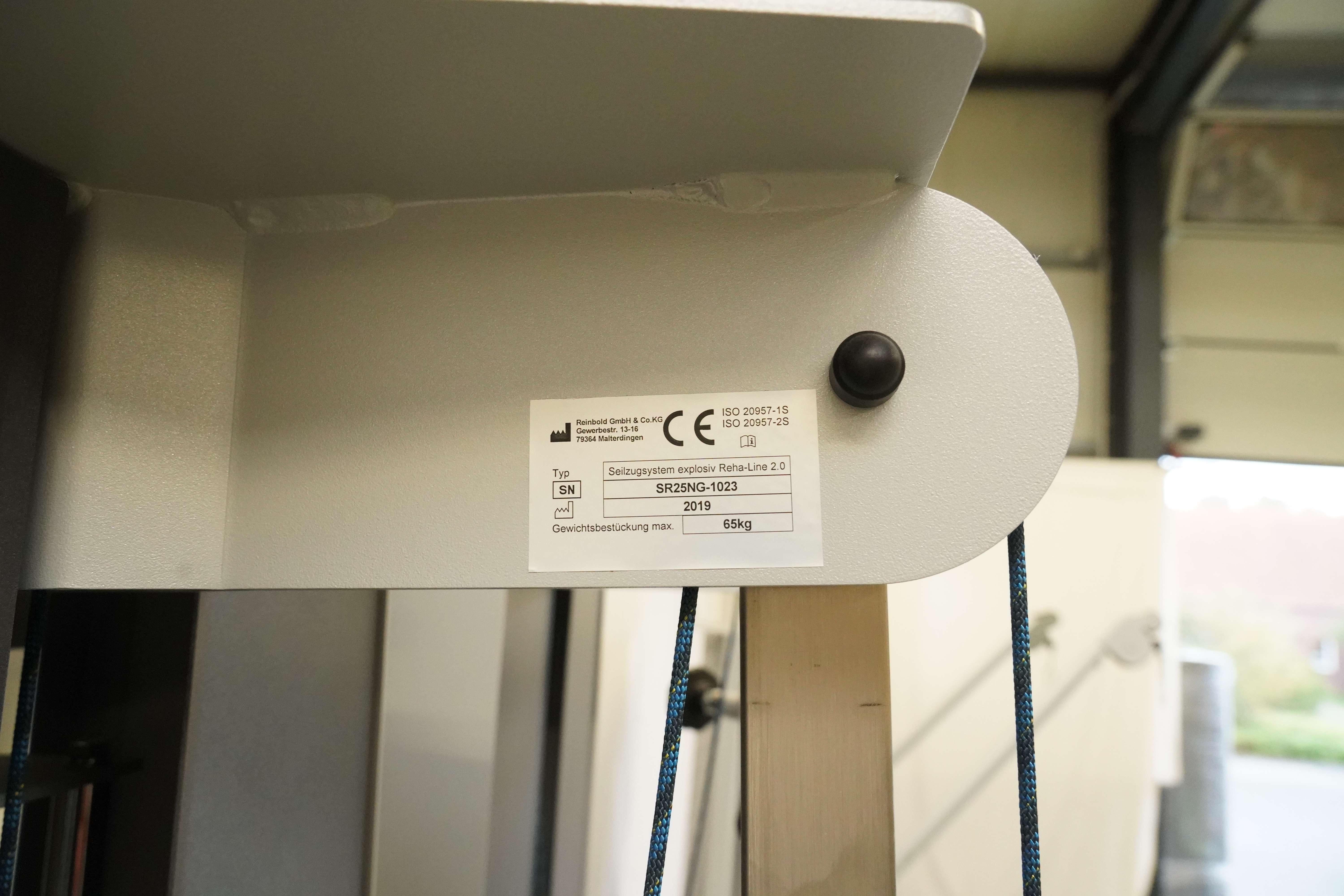 SVG RehaLine 2.0 KG-Gerätesatz: Typenschild mit CE-Kennzeichen an grauem Rahmen, darunter Seile und Holzpfosten