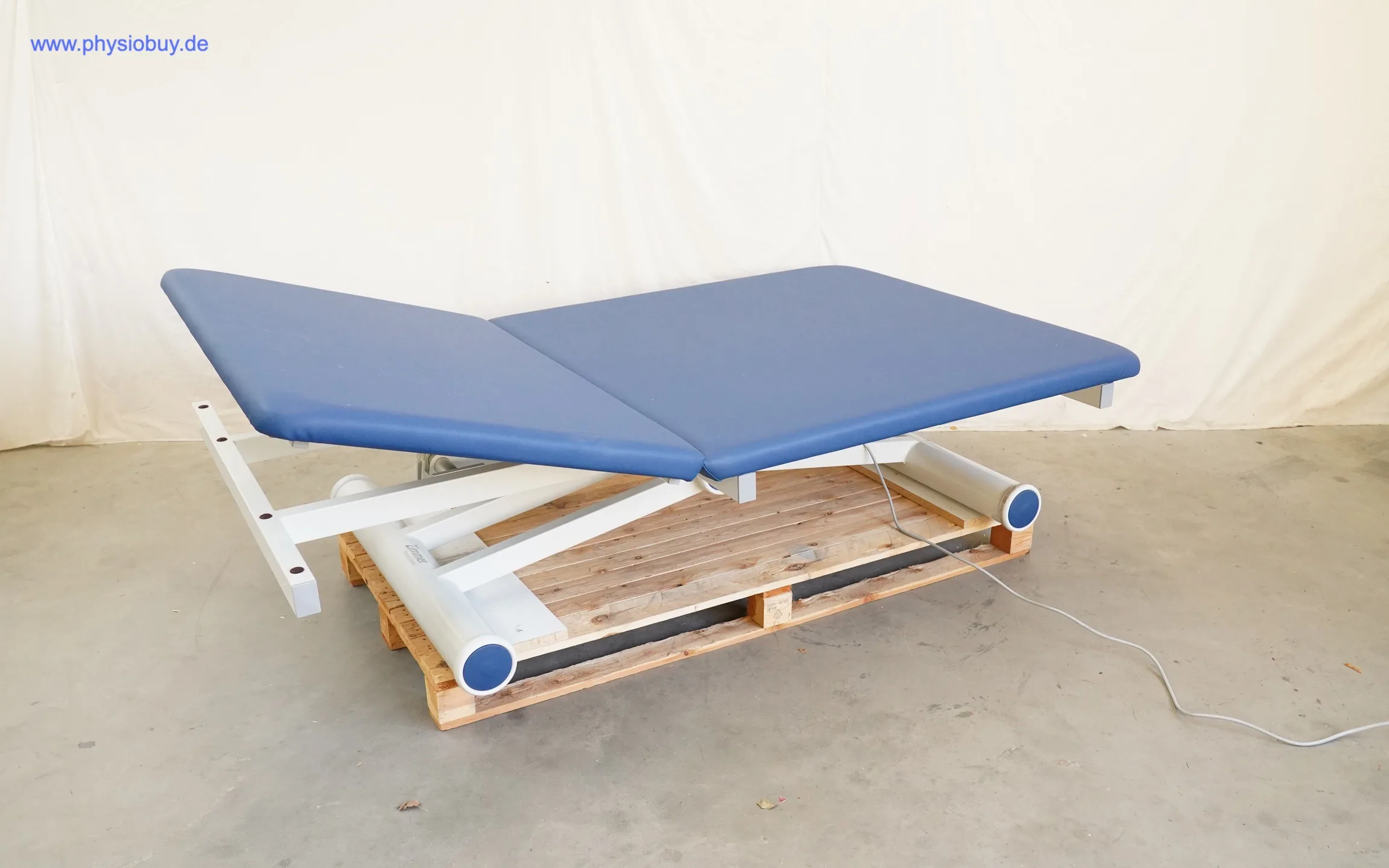 Zimmer aXion Bobath 2 Behandlungsliege in Schrägansicht, blau gepolstert, zweiteilige Liegefläche auf einer Holzpalette