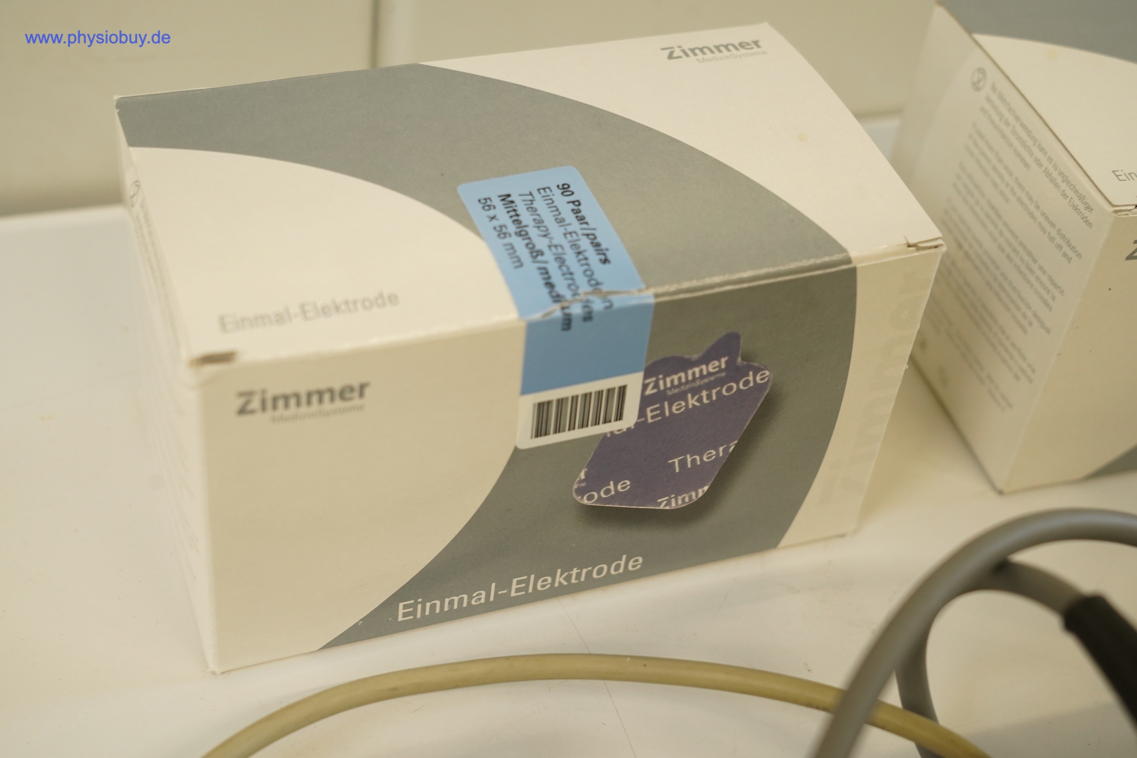 Verpackung von Zimmer Einmal-Elektroden mit Etikett und Barcode, daneben eine weitere Schachtel und ein Kabel