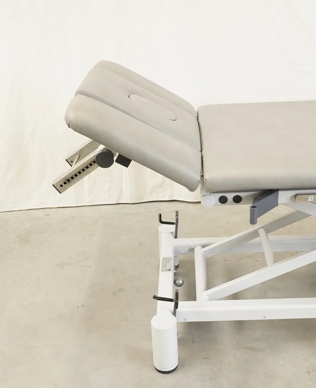 FREI Gym-X (e) Manuell Therapieliege seitlich: hochgestelltes graues Kopfteil mit Lochschiene und weißes Gestell