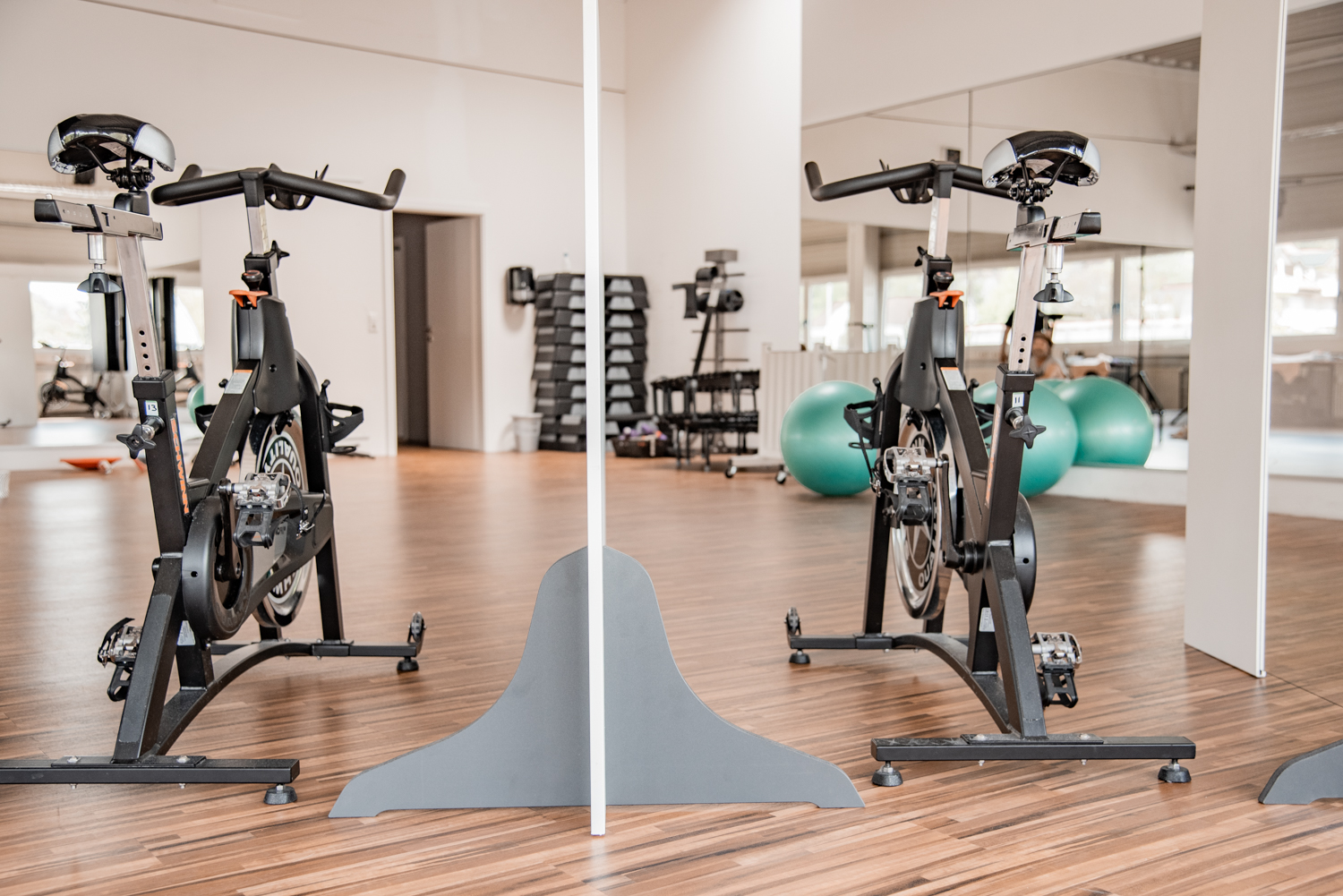Standfuß einer hellgrauen Trennwand Basic zwischen zwei Indoor-Cycles im Spiegel