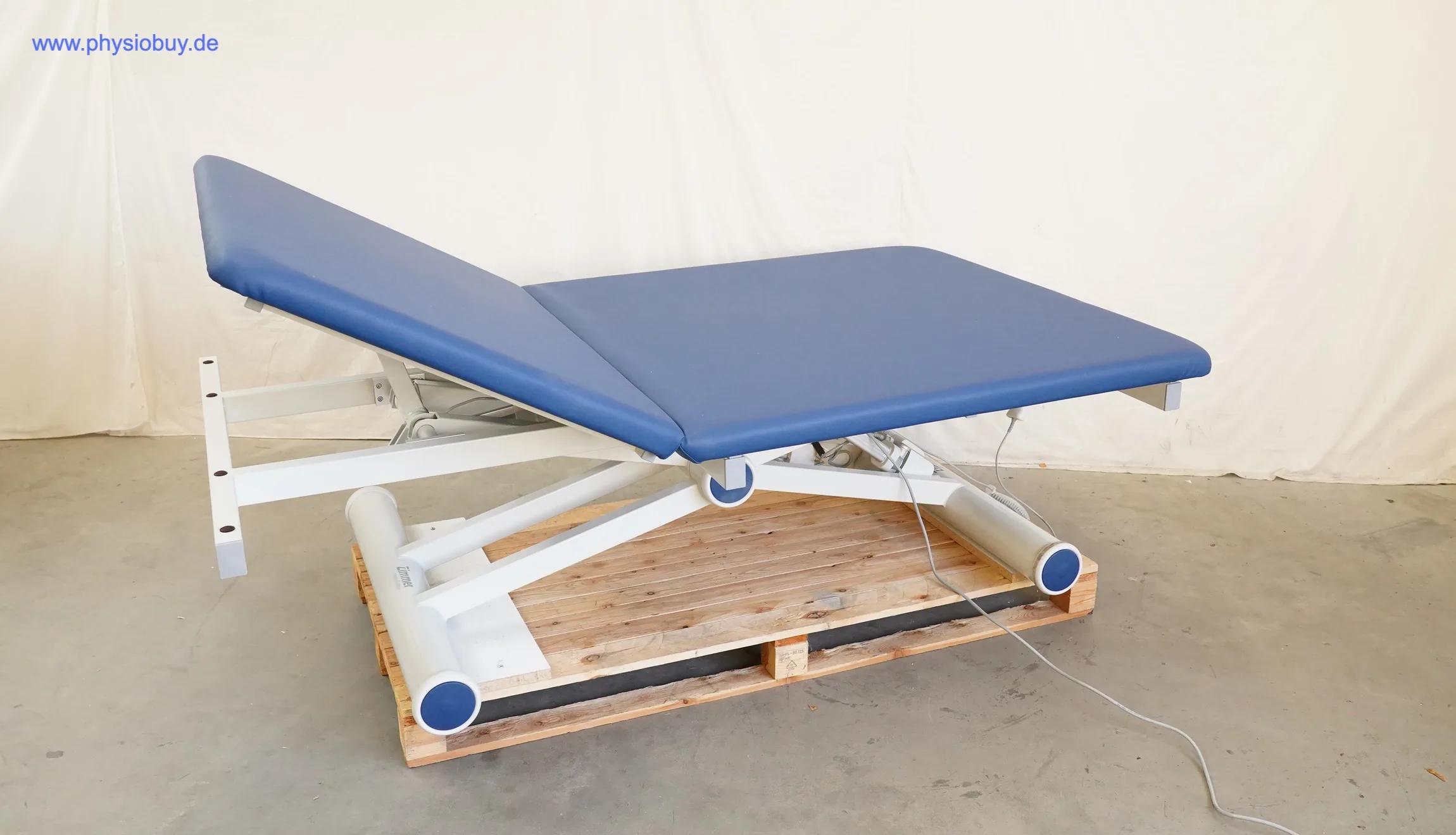 Zimmer aXion Bobath 2 Behandlungsliege schräg von vorn, blaue Polster, Kopfteil angehoben, auf Palette