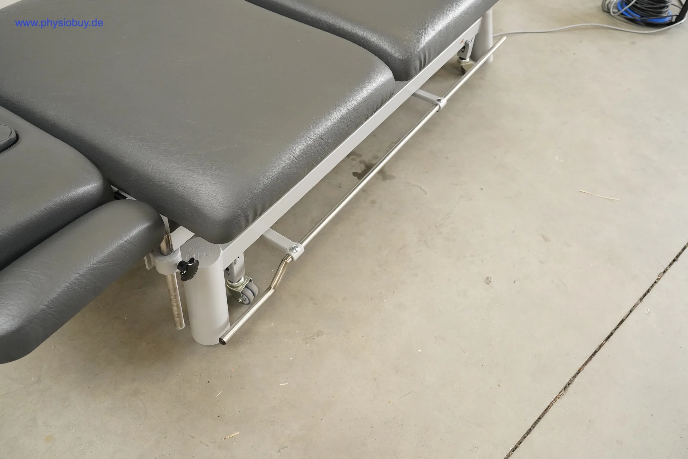 Pino XPert+ Therapieliege, Seitenansicht mit grauen Polstern, Metallrahmen, Haltestange und Fußbügel auf Betonboden