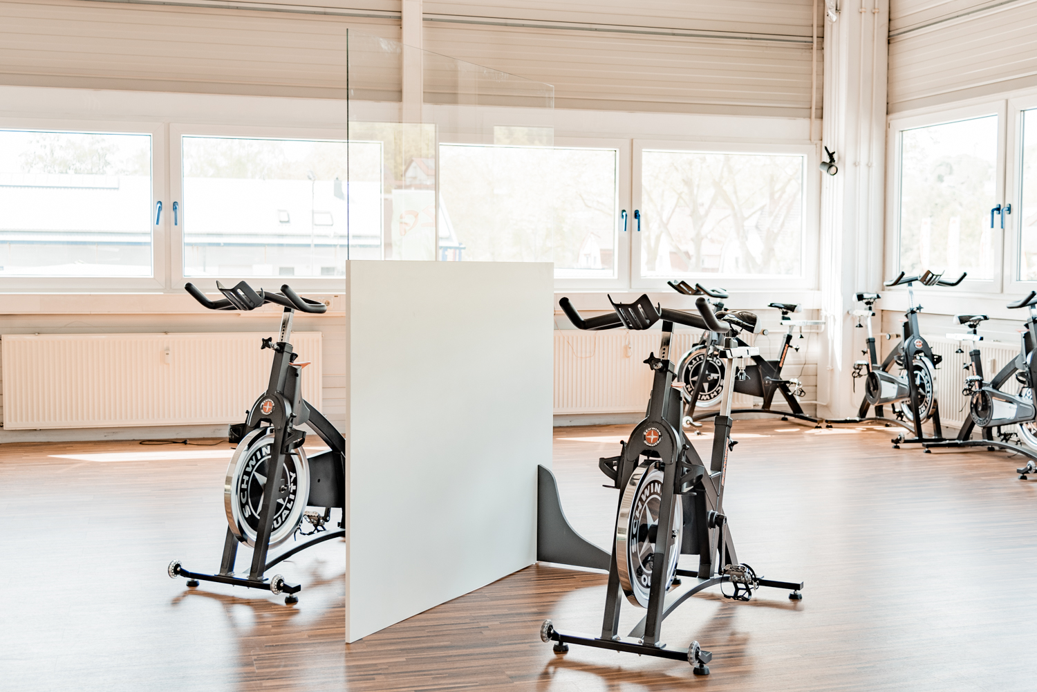 Trennwand Standard mit transparentem Oberteil steht zwischen Indoor-Cycles vor Fensterfront