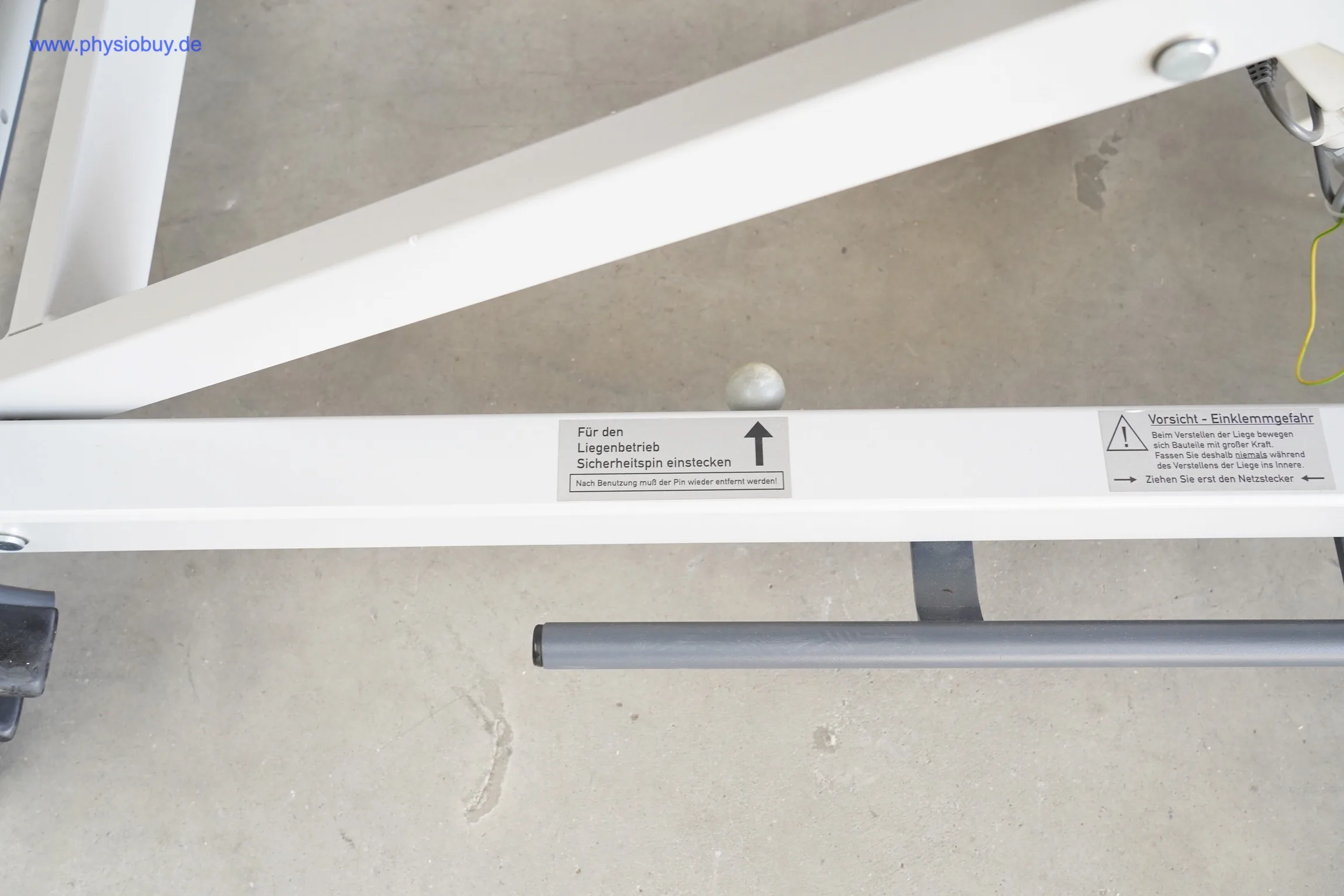 Hinweisschild und Sicherungsstift am Gestell der Behandlungsliege FREI GYM-XII, Nahaufnahme