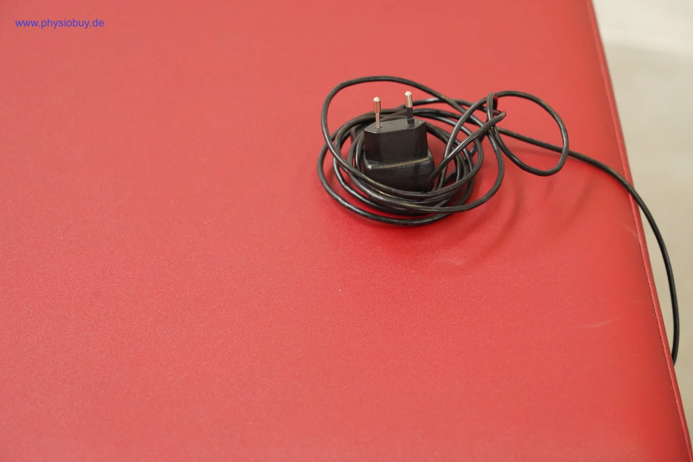 Zimmer Axion Behandlungsliege: aufgerollte Ladekabel mit Netzteil liegt auf der roten Polsterfläche