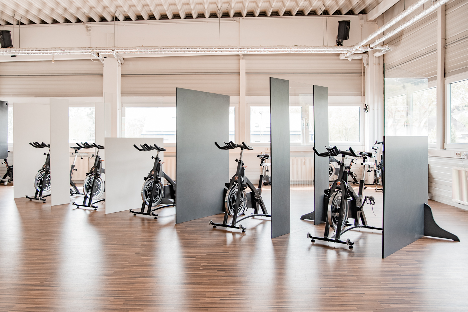 Mehrere Trennwände Exclusive stehen diagonal zwischen einer langen Reihe Indoor-Cycles