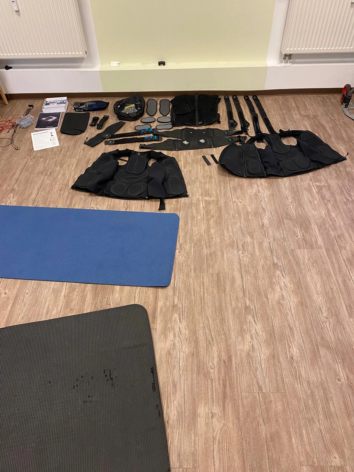 EMS-Westen, Gurte und Kabel des miha-bodytec-Sets ausgebreitet auf dem Boden