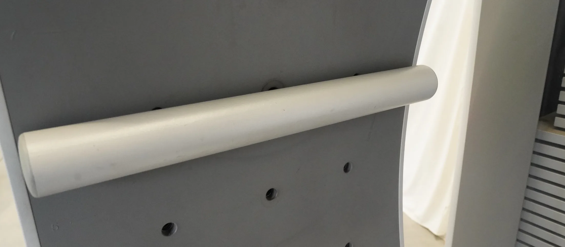 Haltegriff als graues Rundrohr an dunkler Lochplatte eines FREI Genius ECO Geräts, Detailansicht schräg von vorn
