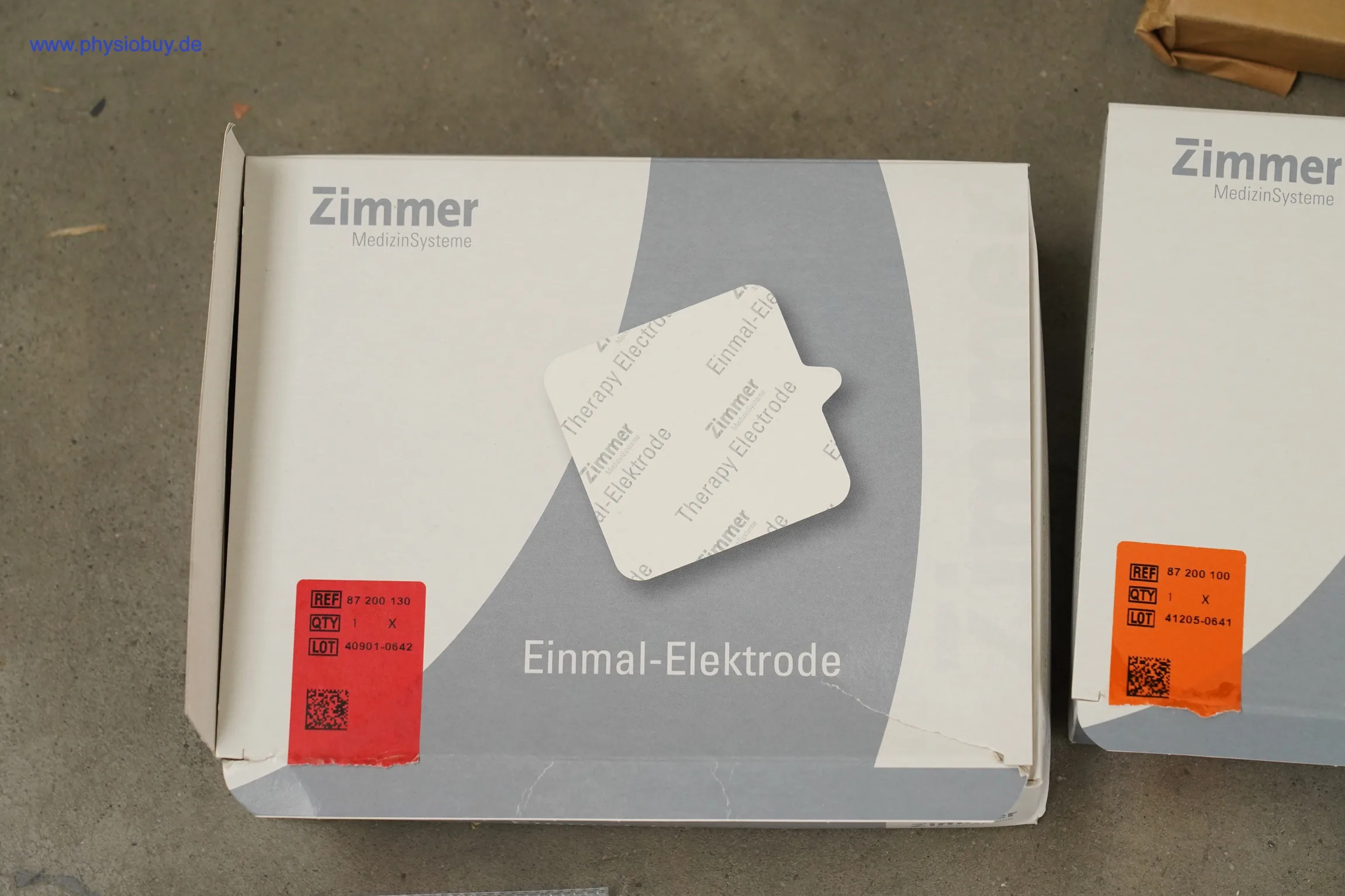 Zimmer Einmal-Elektroden: Verpackung mit rotem Etikett, rechts angeschnitten eine zweite Packung mit orangem Etikett