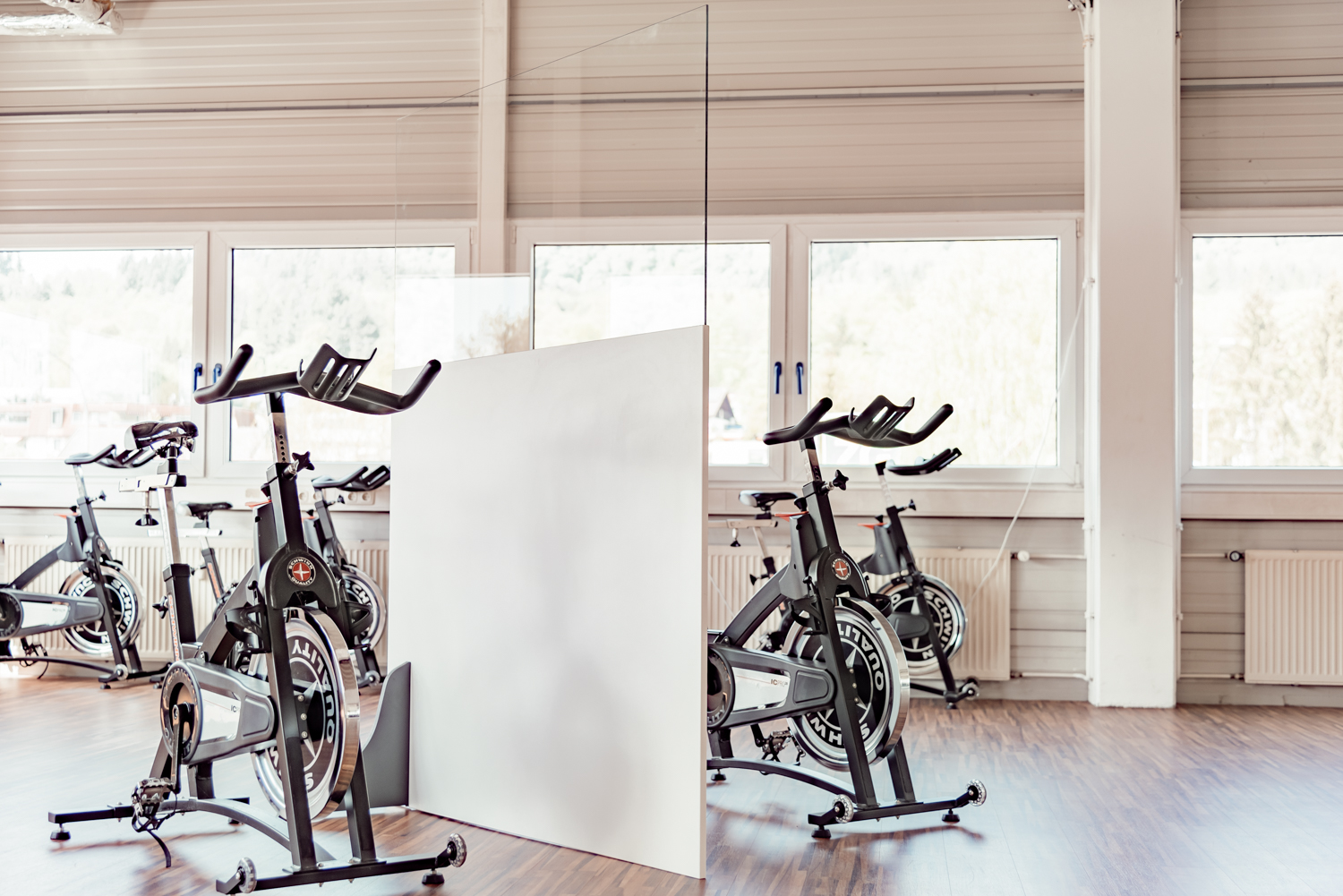 Trennwand Standard mit transparentem Oberteil trennt zwei Reihen Indoor-Cycles vor Fensterfront