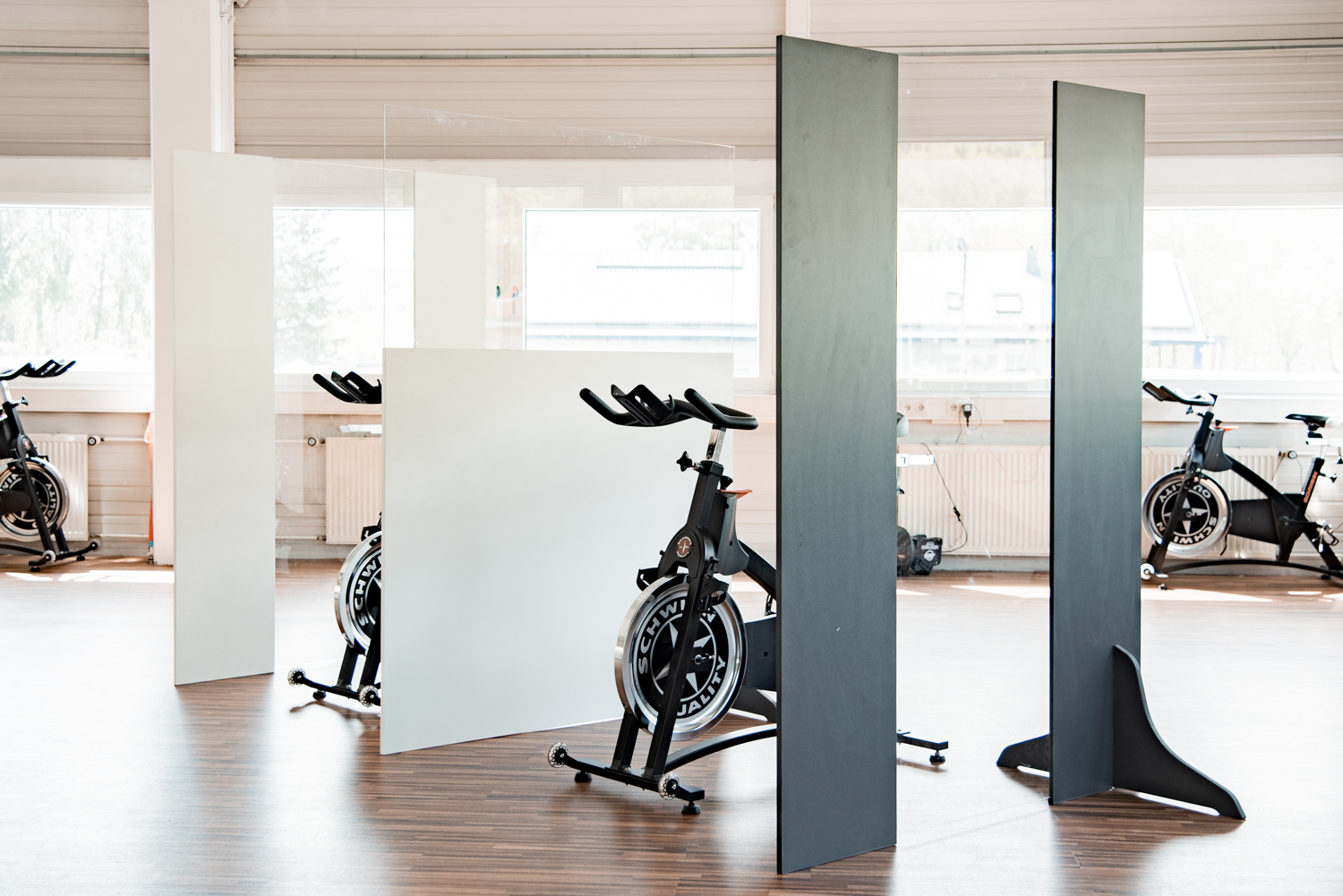 Anthrazitfarbene Trennwände Standard stehen versetzt zwischen Indoor-Cycles im Fitnessstudio