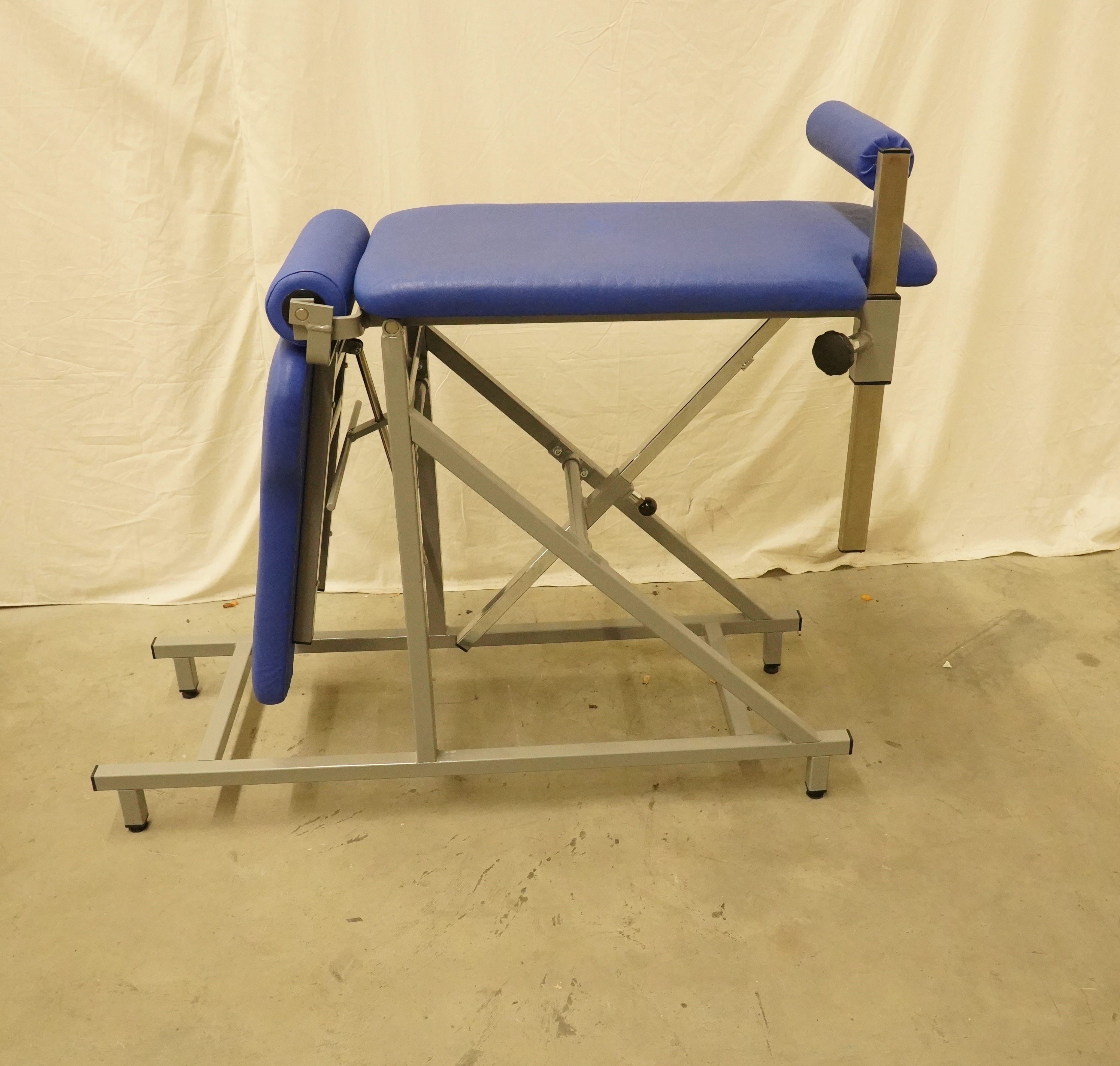 Reinbold Winkeltisch mit blauer Polsterung und grauem Metallgestell in der Seitenansicht, vor hellem Vorhang auf Betonboden