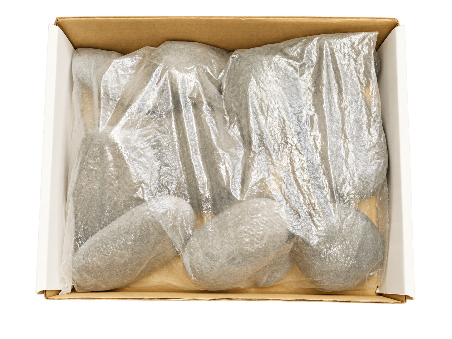 Offener Karton mit in Folie verpackten grauen Massagesteinen für den Hot-Stone-Erhitzer, Ansicht von oben