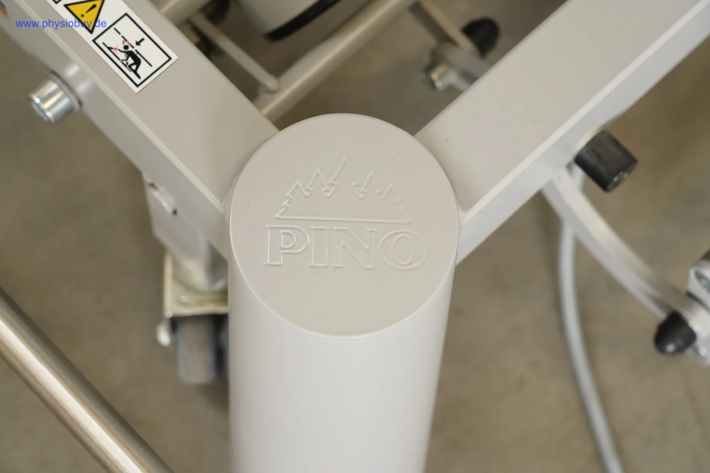 PINO XPert+ Therapieliege, Detail der Rahmenabdeckung mit eingeprägtem PINO-Logo von oben, daneben Rollen und Kabel